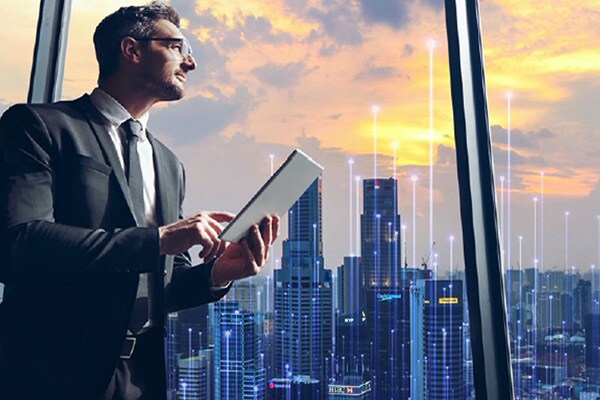 A man looking out of a skyscraper window holding a tab in his hand overlaid with graphics of transmission nodes