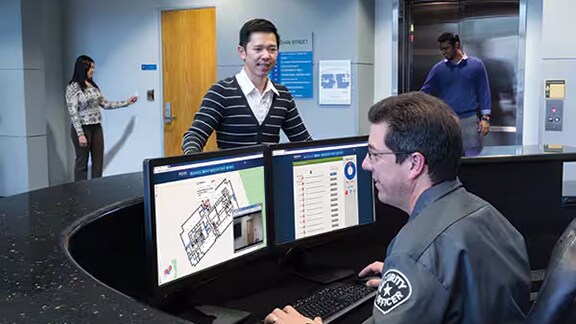 A person talking to the security personnel sitting in the Reception and monitoring the access