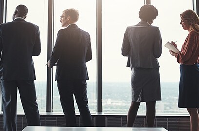Few employees standing  next to glass window in a conference room and discussing work