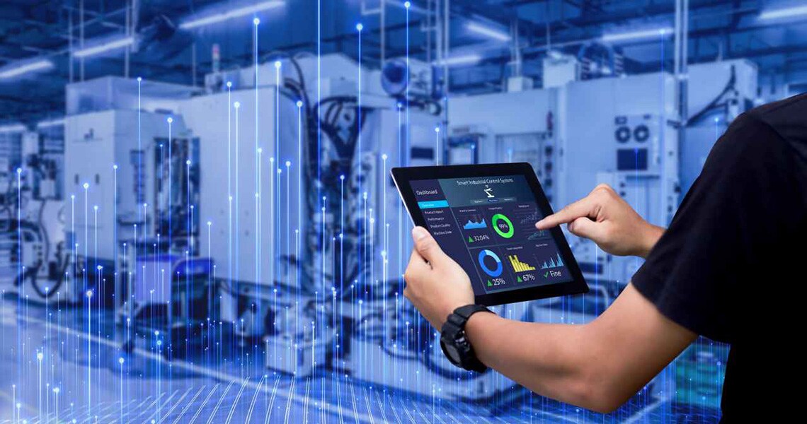 Close up of employee hands analyzing data on the tab with the background view of an industry floor in blue overlaid with graphics of transmission nodes