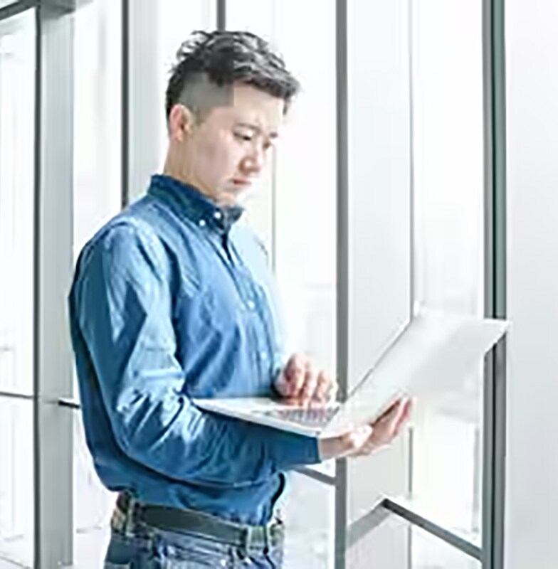 Man standing holding a laptop in his arms in front of full length windows