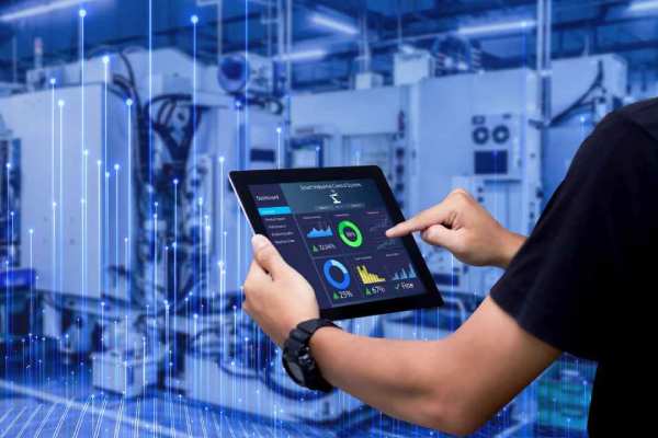 Close up of employee hands analyzing data on the tab with the background view of an industry floor in blue overlaid with graphics of transmission nodes
